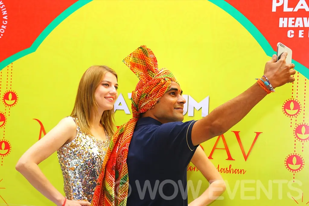 Guest taking a selfie with a performer at the Mahotsav backdrop