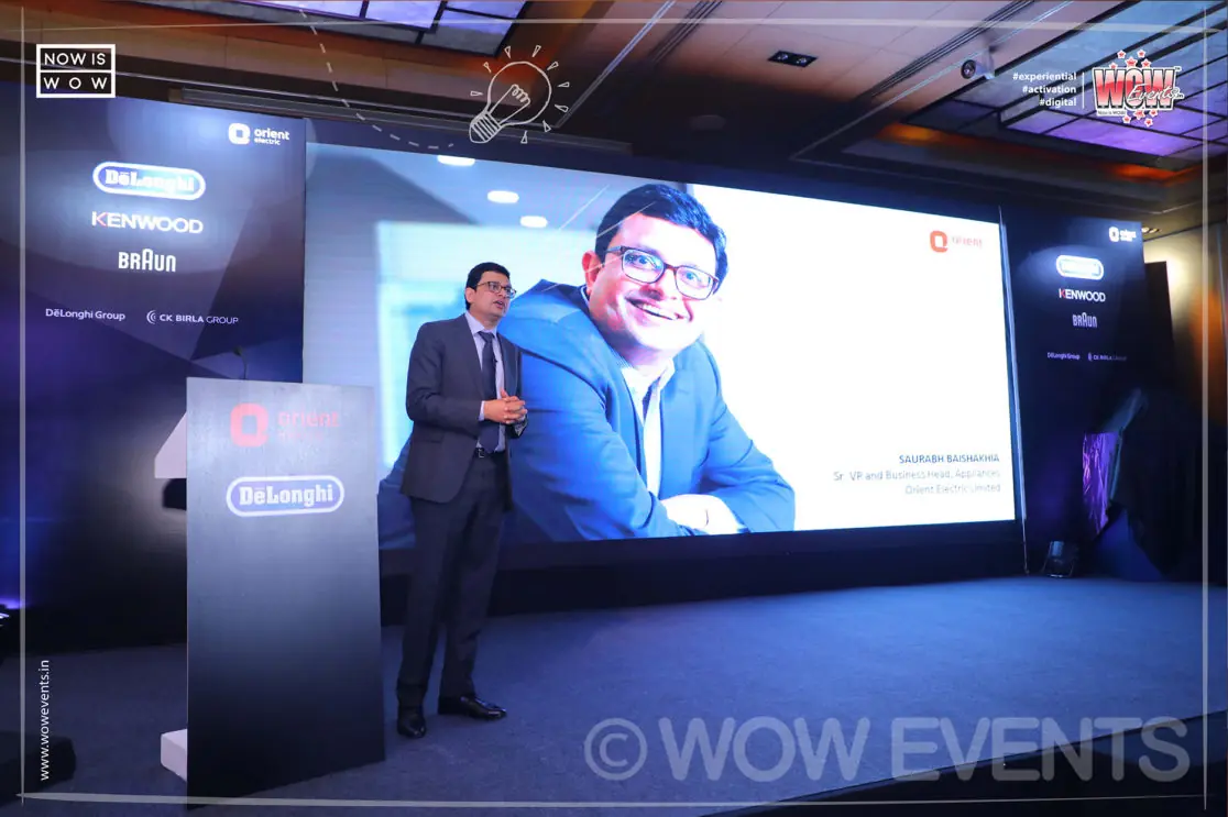 Executive speaking at a podium with his image on screen
