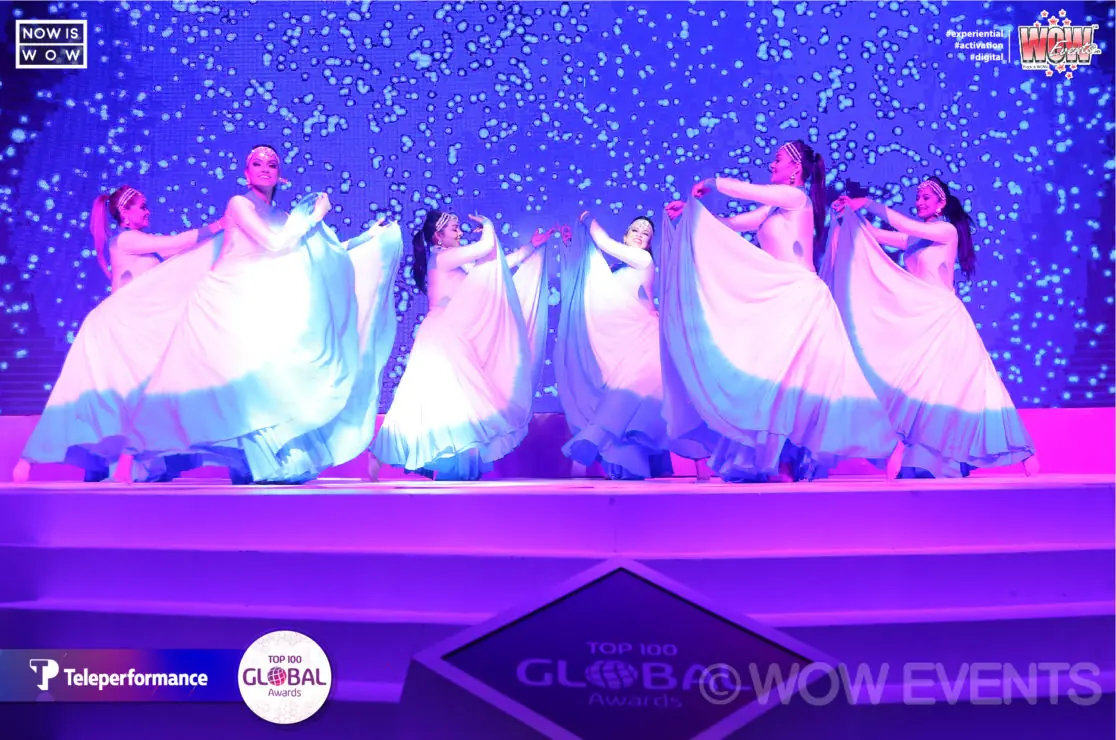 Dancers in white gowns performing under purple lights