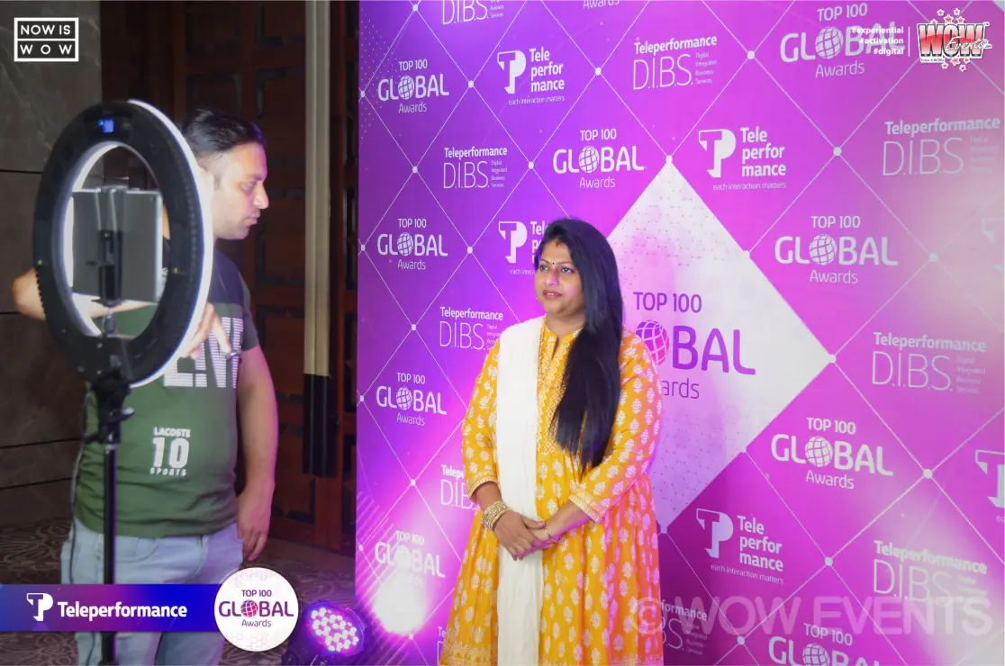 Woman posing with a ring light at the Top 100 Global backdrop
